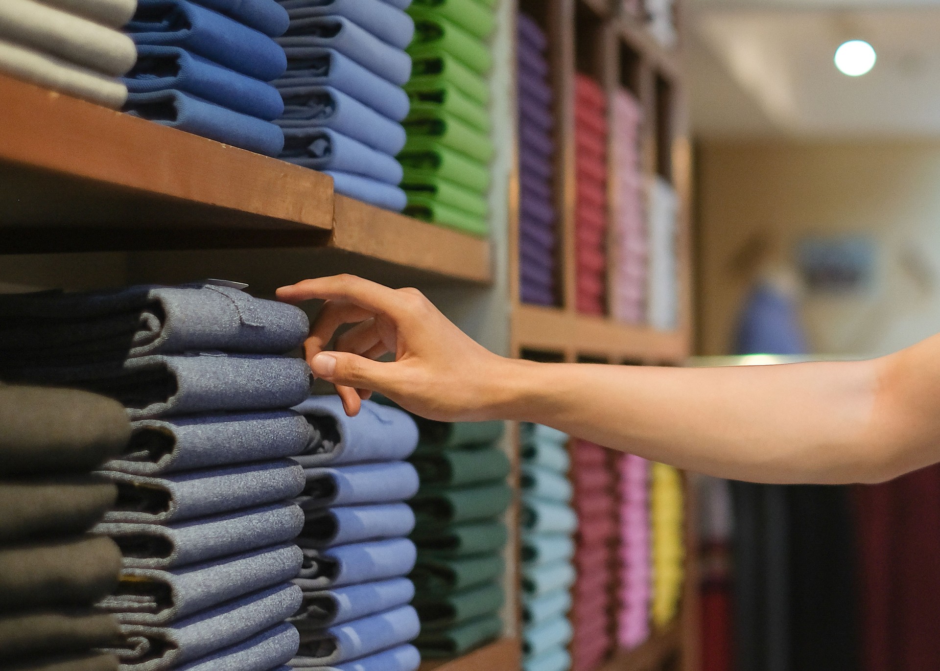 Unrecognizable man  reaching a folded clothes from a store shelf display